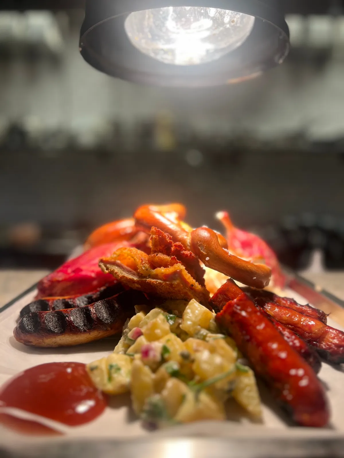 Närbild på grillad korv, schnitzel, kringla och potatissallad under en värmelampa
